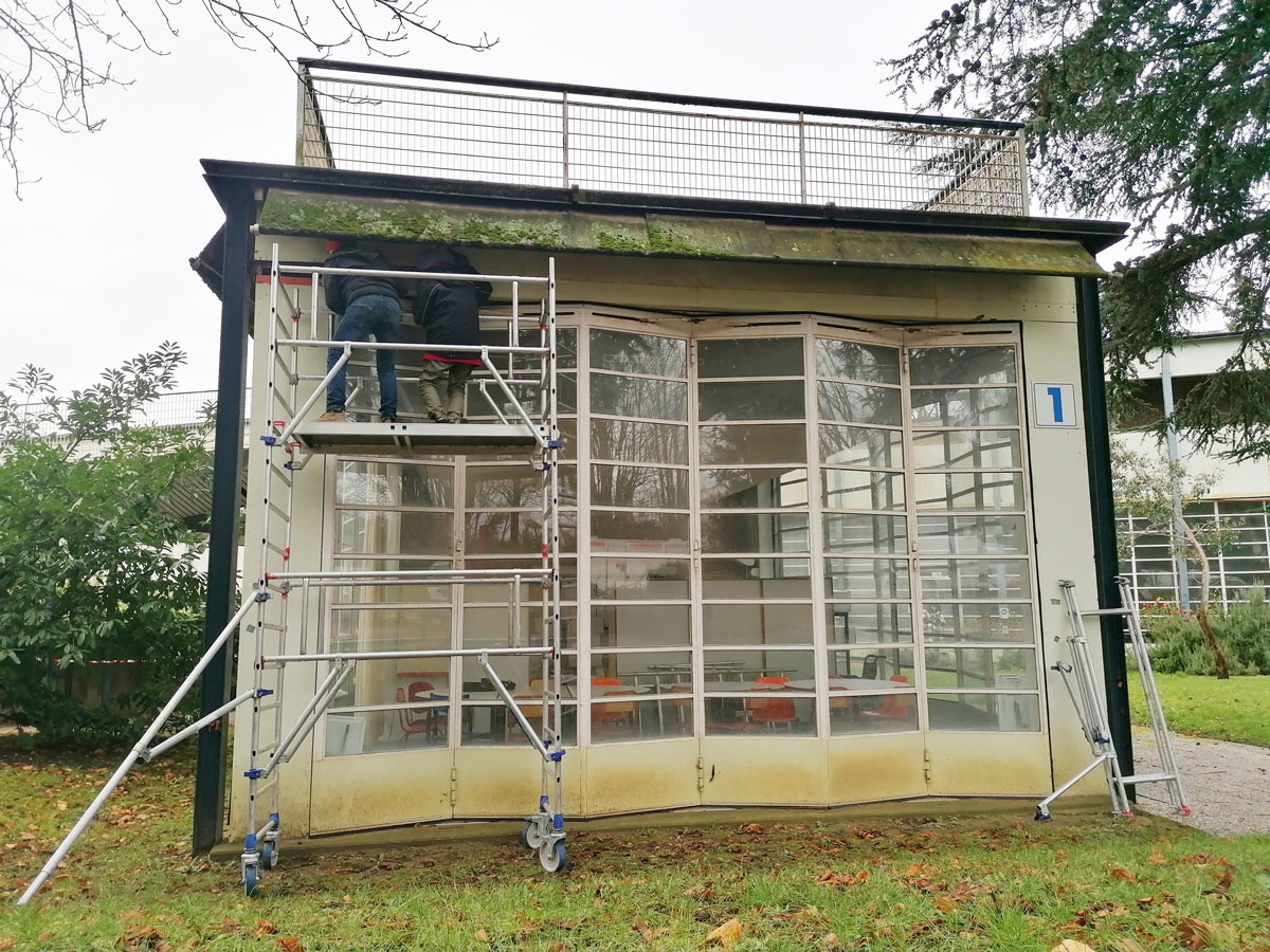 Pavillon de l'école de plein air. Deux hommes, installés sur un échafaudage étudient la structure de la façade en verre. 