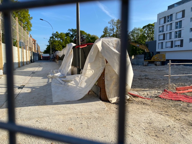 L'intérieur du chantier. Une pelleteuse, une clôture protégée par une bâche.