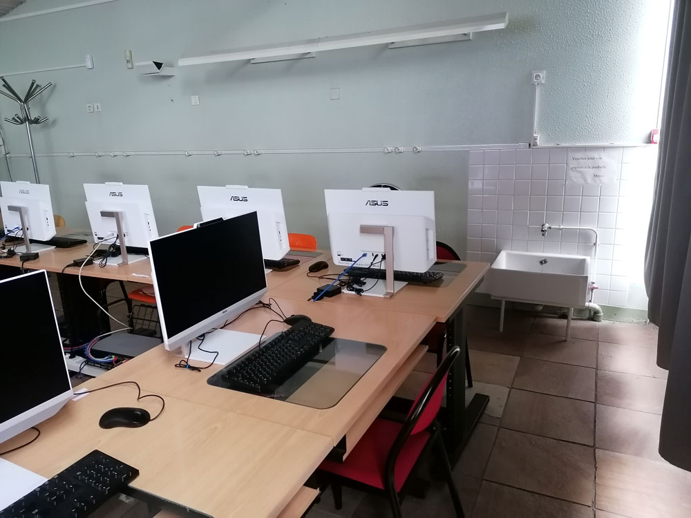 Une salle aves des écrans et des claviers d'ordinateur. Au mur, un petit lavabo. 